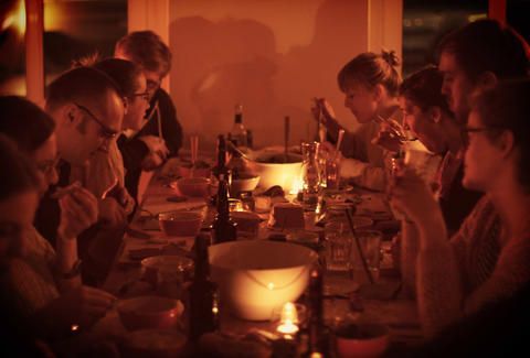 Long candlelit table of guests eating together in warm light