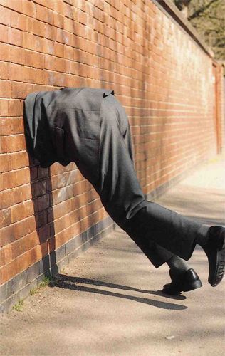 A suited man with his head stuck through a brick wall