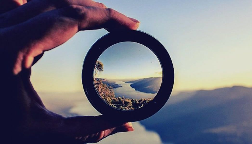 A hand holds a lens ring bringing a hazy river valley into focus