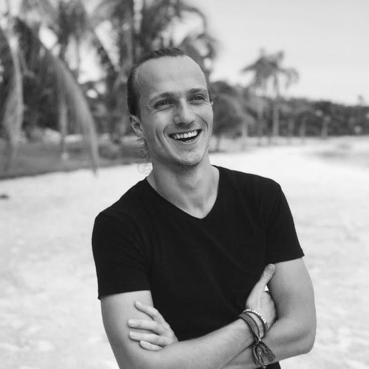 Black and white portrait of Gui smiling on a palm-lined beach